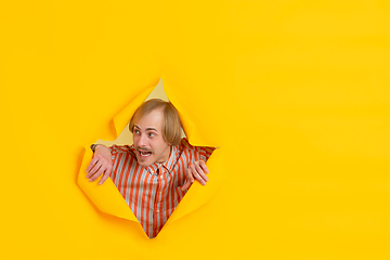 Image showing Cheerful young man poses in torn yellow paper hole background, emotional and expressive