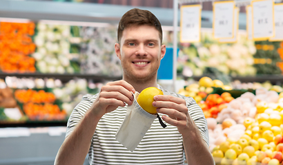 Image showing smiling man putting lemon in reusable grocery tote