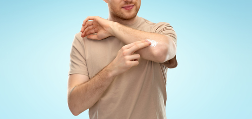 Image showing young man applying pain medication to his elbow