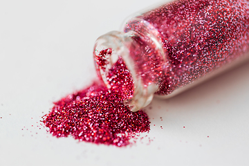 Image showing pink red glitters poured from small glass bottle