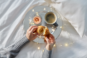 Image showing hands of woman eating croissant with coffee in bed