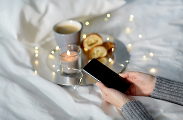 Image showing hands with smartphone, croissant and coffee in bed