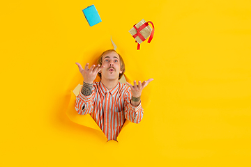 Image showing Cheerful young man poses in torn yellow paper hole background, emotional and expressive