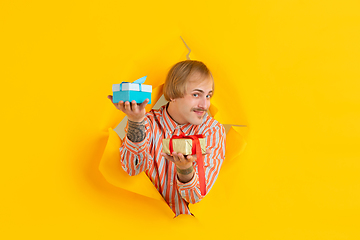 Image showing Cheerful young man poses in torn yellow paper hole background, emotional and expressive