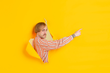 Image showing Cheerful young man poses in torn yellow paper hole background, emotional and expressive