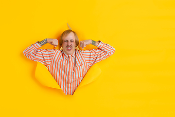 Image showing Cheerful young man poses in torn yellow paper hole background, emotional and expressive