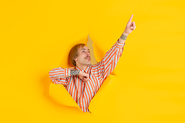 Image showing Cheerful young man poses in torn yellow paper hole background, emotional and expressive