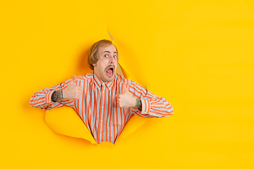 Image showing Cheerful young man poses in torn yellow paper hole background, emotional and expressive