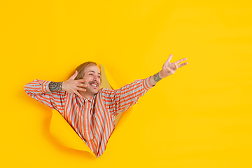 Image showing Cheerful young man poses in torn yellow paper hole background, emotional and expressive