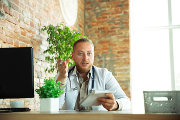 Image showing Caucasian doctor consulting for patient, explaining recipe for drug, working in cabinet