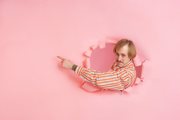 Image showing Cheerful young man poses in torn coral paper hole background, emotional and expressive