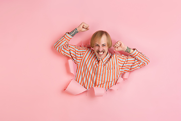 Image showing Cheerful young man poses in torn coral paper hole background, emotional and expressive