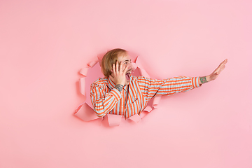 Image showing Cheerful young man poses in torn coral paper hole background, emotional and expressive