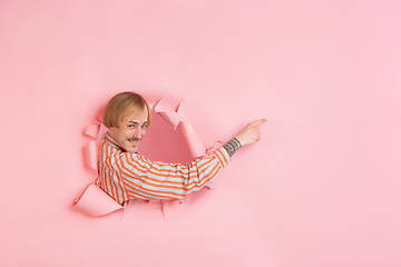 Image showing Cheerful young man poses in torn coral paper hole background, emotional and expressive