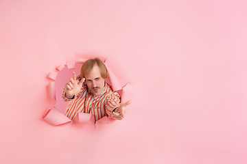 Image showing Cheerful young man poses in torn coral paper hole background, emotional and expressive