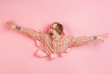 Image showing Cheerful young man poses in torn coral paper hole background, emotional and expressive