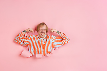 Image showing Cheerful young man poses in torn coral paper hole background, emotional and expressive