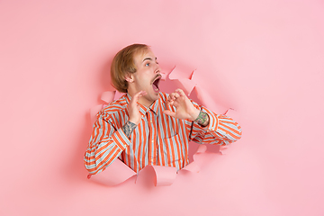 Image showing Cheerful young man poses in torn coral paper hole background, emotional and expressive