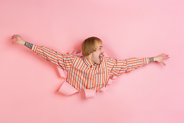 Image showing Cheerful young man poses in torn coral paper hole background, emotional and expressive