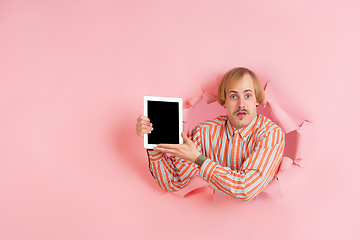 Image showing Cheerful young man poses in torn coral paper hole background, emotional and expressive