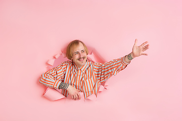 Image showing Cheerful young man poses in torn coral paper hole background, emotional and expressive