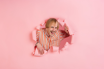 Image showing Cheerful young man poses in torn coral paper hole background, emotional and expressive