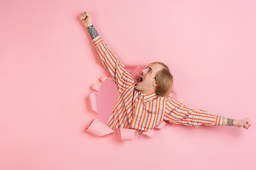 Image showing Cheerful young man poses in torn coral paper hole background, emotional and expressive