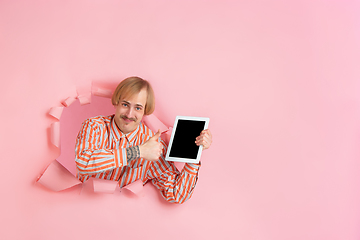 Image showing Cheerful young man poses in torn coral paper hole background, emotional and expressive