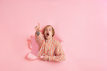 Image showing Cheerful young man poses in torn coral paper hole background, emotional and expressive