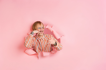 Image showing Cheerful young man poses in torn coral paper hole background, emotional and expressive