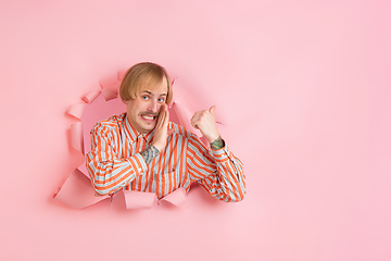 Image showing Cheerful young man poses in torn coral paper hole background, emotional and expressive