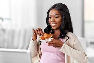 Image showing woman with laptop eating croissant at home office