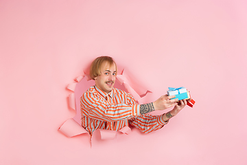 Image showing Cheerful young man poses in torn coral paper hole background, emotional and expressive