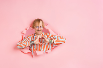 Image showing Cheerful young man poses in torn coral paper hole background, emotional and expressive