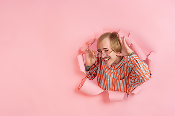 Image showing Cheerful young man poses in torn coral paper hole background, emotional and expressive