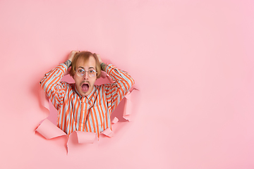 Image showing Cheerful young man poses in torn coral paper hole background, emotional and expressive