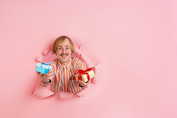 Image showing Cheerful young man poses in torn coral paper hole background, emotional and expressive