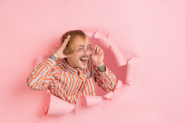 Image showing Cheerful young man poses in torn coral paper hole background, emotional and expressive