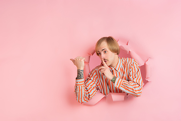 Image showing Cheerful young man poses in torn coral paper hole background, emotional and expressive