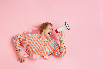 Image showing Cheerful young man poses in torn coral paper hole background, emotional and expressive