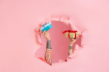 Image showing Male hand giving gift in torn coral paper hole background, celebration