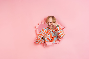 Image showing Cheerful young man poses in torn coral paper hole background, emotional and expressive