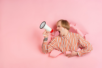 Image showing Cheerful young man poses in torn coral paper hole background, emotional and expressive