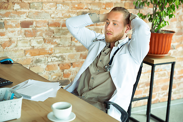 Image showing Caucasian doctor resting after consulting for patient, working in cabinet