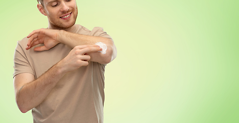 Image showing young man applying pain medication to his elbow