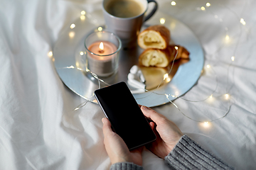 Image showing hands with smartphone, croissant and coffee in bed