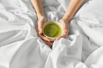 Image showing hands of woman with cup of matcha tea in bed