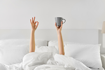 Image showing woman with cup of coffee lying in bed showing ok