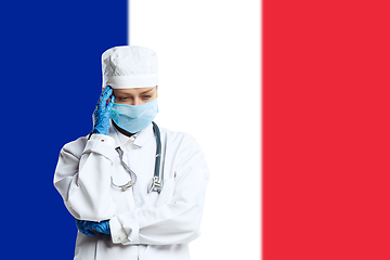 Image showing Female young doctor with stethoscope and face mask praying for God with France national flag on background