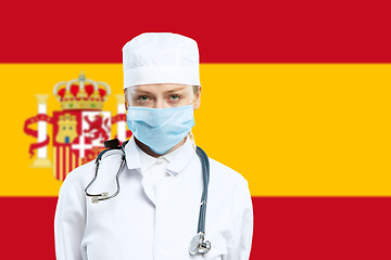 Image showing Female young doctor with stethoscope and face mask praying for God with Spain national flag on background